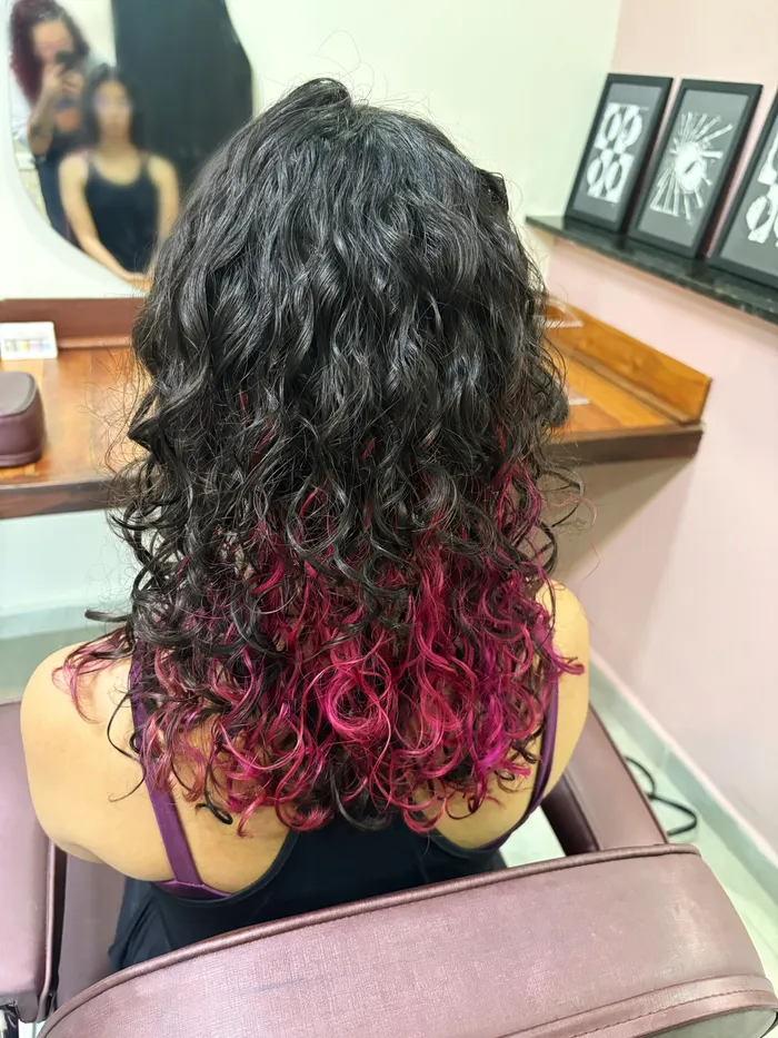 Cabelo cacheado escuro com as pontas coloridas de rosa, visto de trás, no Awá Lab